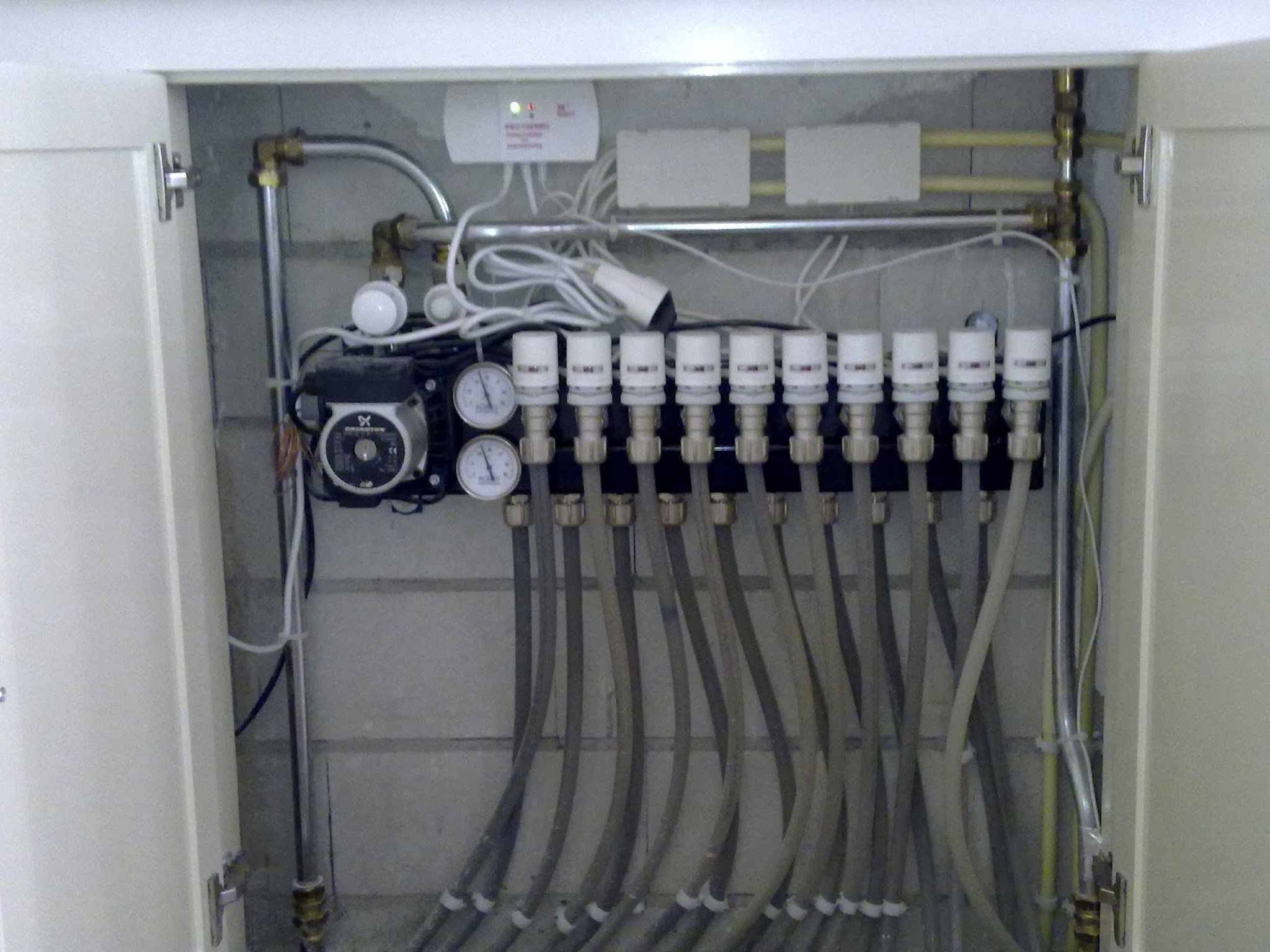 Verdeler voor vloerverwarming in een wandkast, met tien groepen, twee manometers en een Grundfos pomp
