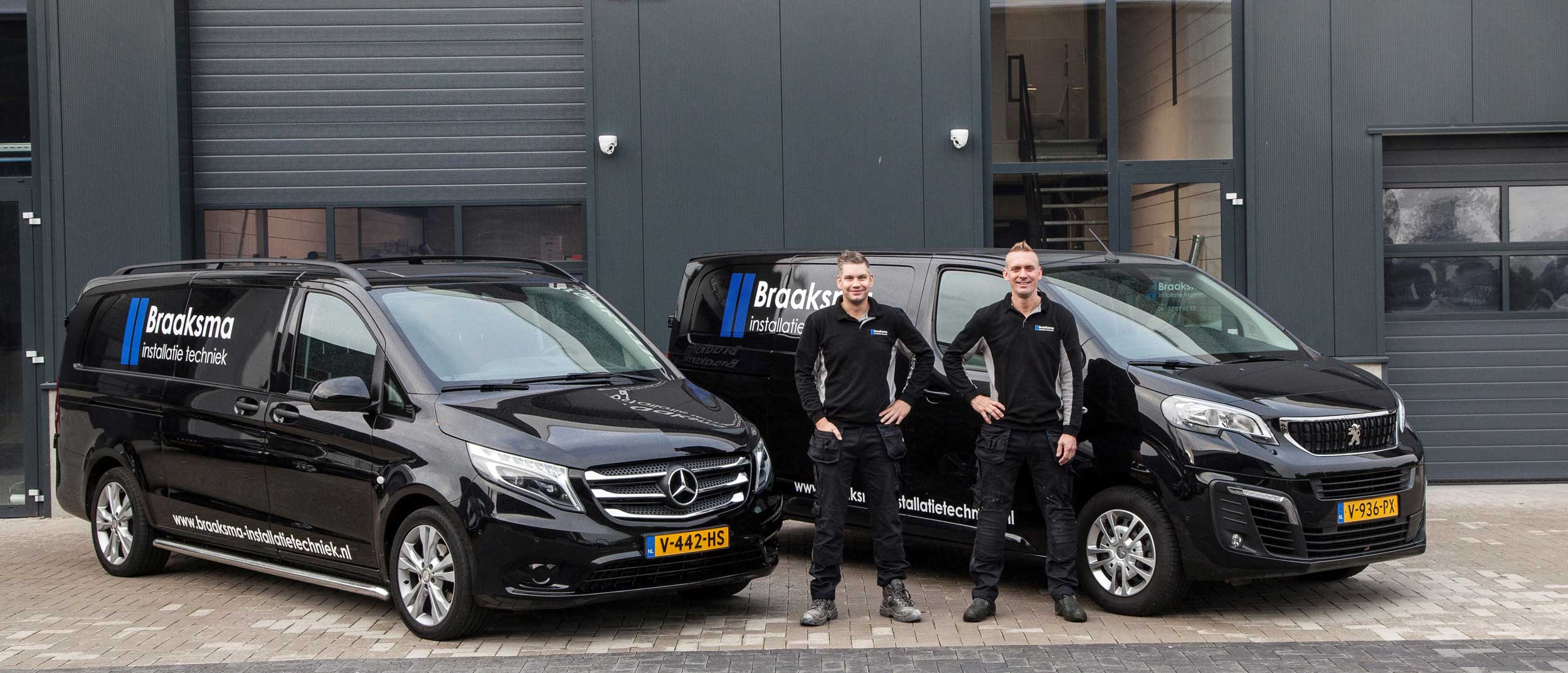 Twee monteurs van Braaksma Installatietechniek in bedrijfskleding voor hun twee bedrijfsbussen